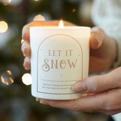 a person holding a lit candle in front of a christmas tree that says let it snow