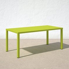 a green table sitting on top of a cement floor next to a white wall in an empty room