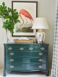 a green dresser with a pink flamingo painting on the wall above it and a lamp next to it