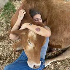 a woman is hugging a cow on the ground with her arm around it's head