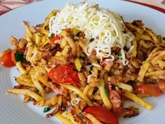 a white plate topped with pasta and meat covered in cheese, tomatoes and parmesan sprinkles