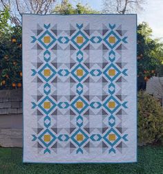 a quilted wall hanging on the side of a house with an orange tree in the background