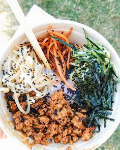 a person holding up a white bowl filled with different types of food and chopsticks