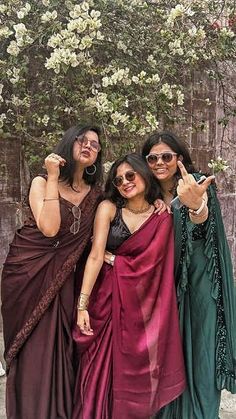 three women pose for the camera in front of a tree with white flowers on it