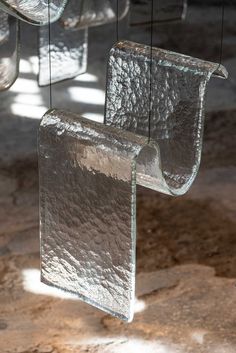 several glass objects hanging from strings in a room with concrete flooring and light shining on them