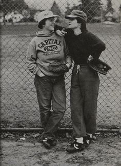 an old black and white photo of two people standing in front of a chain link fence