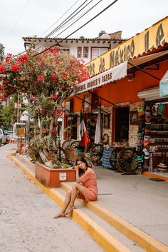 a woman sitting on the curb talking on her cell phone in front of a store