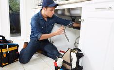 a man fixing an appliance in his kitchen under the sink with tools on the floor