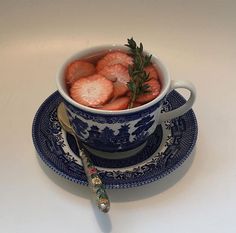 a blue and white bowl filled with strawberries on top of a plate next to a spoon