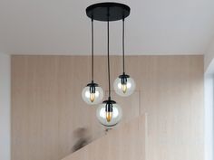 three light bulbs hanging from the ceiling in a room with wood paneling and stairs