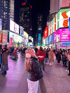 a woman standing in the middle of a busy city street at night with lots of people