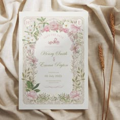 a wedding card with pink flowers and greenery on top of a white cloth covered bed