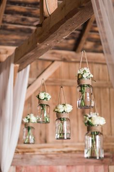 hanging mason jars filled with white flowers and greenery are the focal point for this rustic wedding