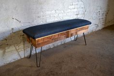 a wooden bench with hairpin legs and a black cushion on the seat is against a white brick wall