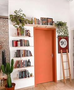 an orange door in a white room with bookshelves and plants on the shelves