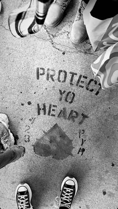 black and white photograph of people standing on sidewalk with words written on the pavement that read protect you heart