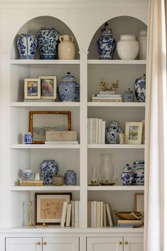 a white bookcase filled with blue and white vases