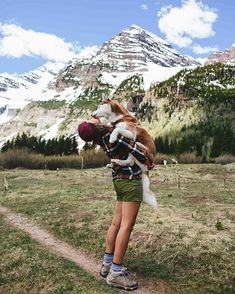 a woman holding a dog in her arms on the side of a dirt road with mountains in the background