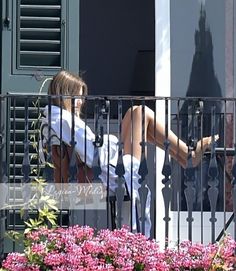 a woman is sitting on the balcony with her legs spread out and looking at something