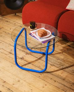 a glass table with a croissant sitting on top of it next to a red couch