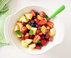 a white bowl filled with fruit on top of a table next to a green napkin