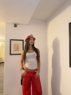 a woman wearing red pants and a white tank top standing in front of a wall