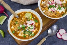 two bowls of soup with meat, onions and cilantro on a cutting board