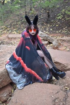 a woman dressed up as a demon sitting on rocks