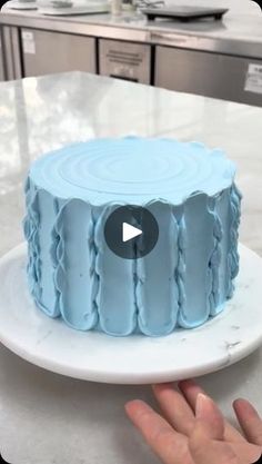 a blue cake sitting on top of a white plate next to a person's hand