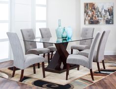 a glass dining table with grey chairs around it and a rug in front of the table