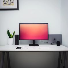 a desktop computer sitting on top of a white desk next to a phone and potted plant