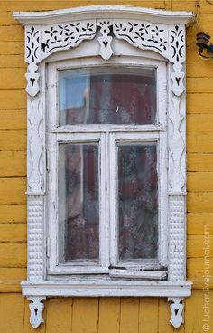 an old window on the side of a yellow building with white trim and ornate decorations