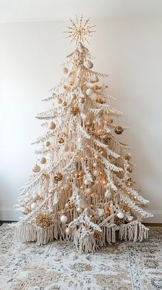 a white christmas tree with gold ornaments and fringes on the bottom is standing in front of a wall