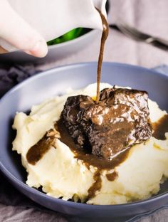 someone pouring chocolate sauce over mashed potatoes in a blue bowl