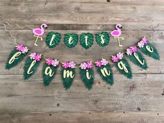 some pink flamingos and green leaves are hanging on a wooden wall with the words happy flamingo