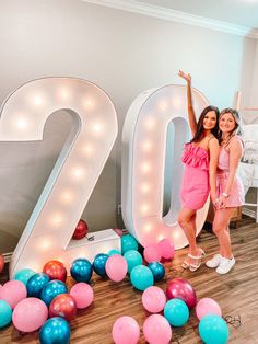 two girls standing next to the number twenty and balloons