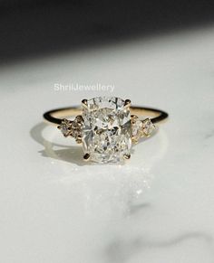 an oval cut diamond ring with three smaller diamonds on the band, set in 18k yellow gold