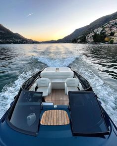 the back end of a boat traveling on water with mountains in the background at sunset