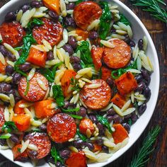 a white bowl filled with pasta, beans and sausage on top of a wooden table