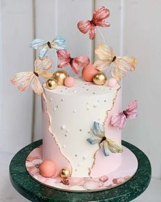 a white cake with pink, blue and gold decorations on top is sitting on a green plate