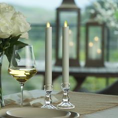 a glass of wine next to two candles on a table with flowers in the background