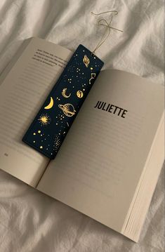 an open book sitting on top of a bed next to a white sheet with stars and planets