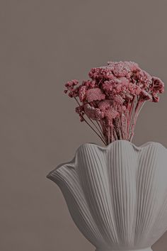 a white vase filled with pink flowers on top of a table