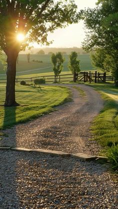 the sun shines brightly on a gravel road leading to a fenced in field