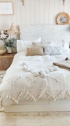 a white bed with pillows and blankets on top of it in a bedroom next to a wicker basket