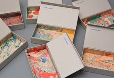 six open boxes with different colored papers in them on a gray surface, one opened and the other closed