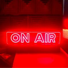 a red neon sign that says on air in front of a dresser with drawers and lamps