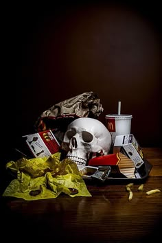 a skull sitting on top of a wooden table next to chips and a hot dog