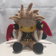 a crocheted stuffed animal sitting on top of a white plate with red and yellow wings