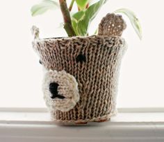 a plant in a knitted pot sitting on a window sill with a teddy bear face